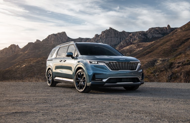 The 2021 Kia Carnival parked near some mountains.