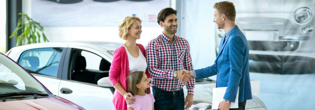 A couple shaking hands with a car salesman