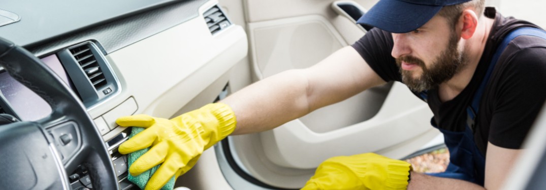 A man with gloves on cleaning the inside of a car