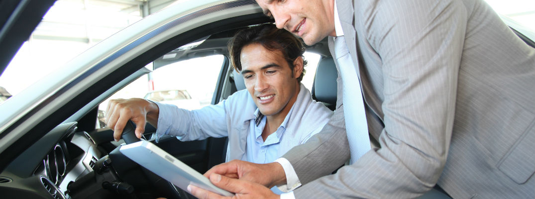 A stock photo of a customer learning about a vehicle with a sales person.