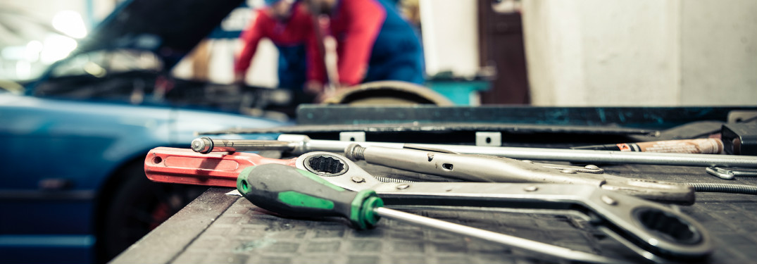 tools in foreground and mechanics in background working on car
