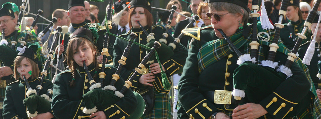 A stock photo of people playing bagpipes in a St. Patrick's Day parade.