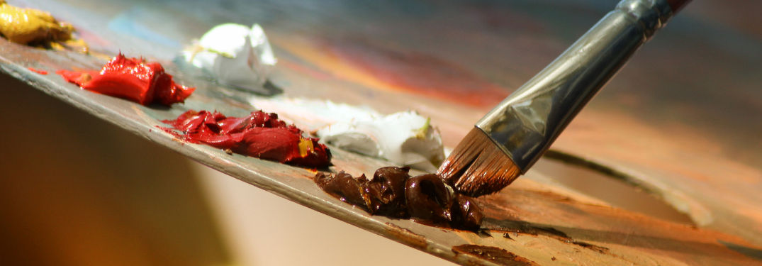 A paintbrush getting brown paint off of a tray
