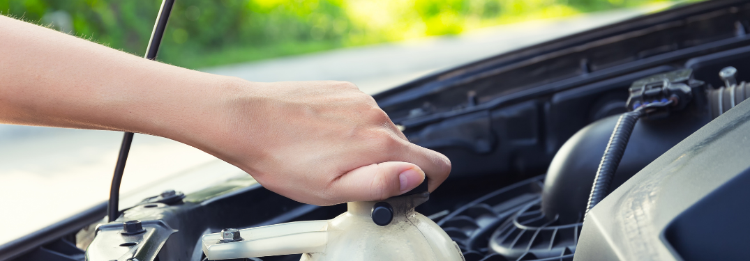 A hand unscrewing a coolant cap