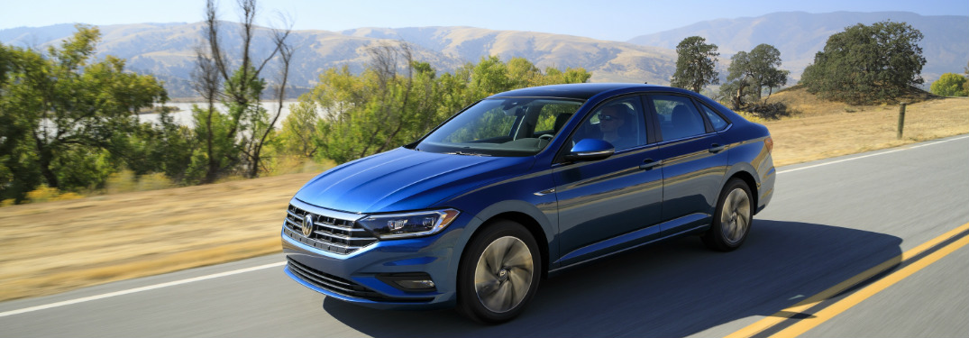 2019 Volkswagen Jetta in blue driving near a lake surrounded by mountains