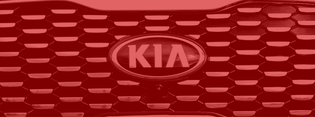 Red tinted image of a Kia vehicle's front grille and badge