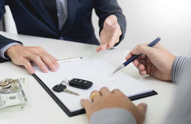 Person signing paperwork for a new vehicle with keys on the table