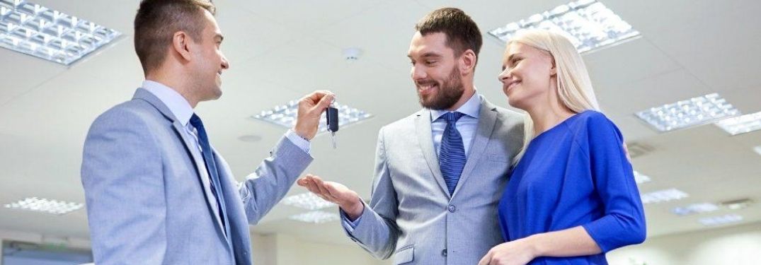 Car Salesman Handing Car Keys to a Young Couple in a Dealership