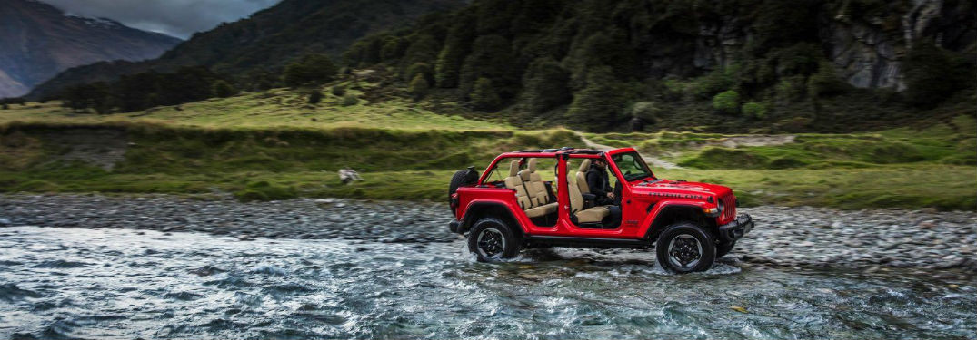 Red 2018 Jeep Wrangler driving through a stream with doors removed