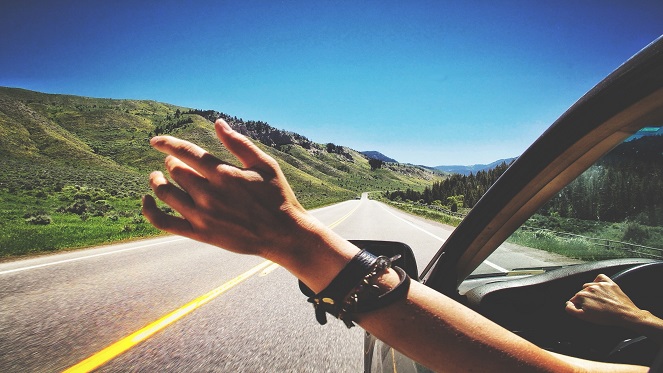 A Lady has her hand out as she enjoys the open road during her road trip