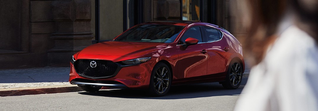 A red 2020 Mazda3 Hatchback parked at a traffic sign in the middle of an urban area.