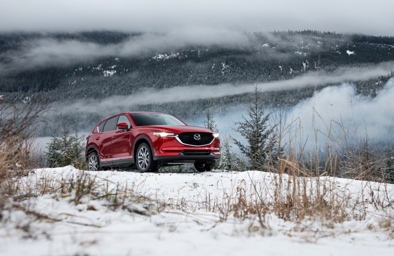 A red 2020 Mazda CX-5 driving over a snowy hill.