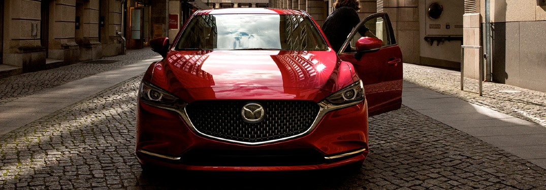 A red 2020 Mazda6 parked on a cobblestone road with the driver getting out of the vehicle.