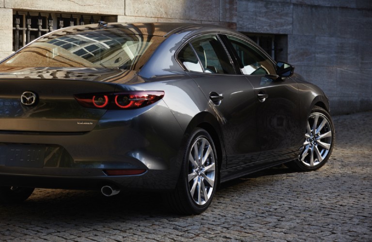 The rear and side view of a gray 2021 Mazda3 Sedan parked on a cobblestone street.