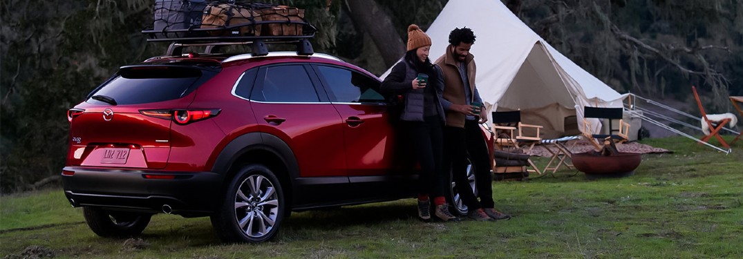 A couple sitting on a red 2021 Mazda CX-30 while out camping.