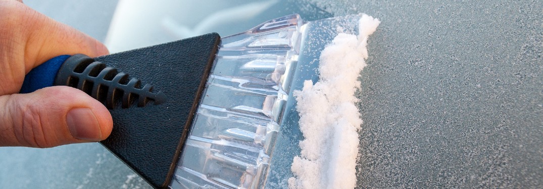 A person using a window scraper to take ice off a windshield.