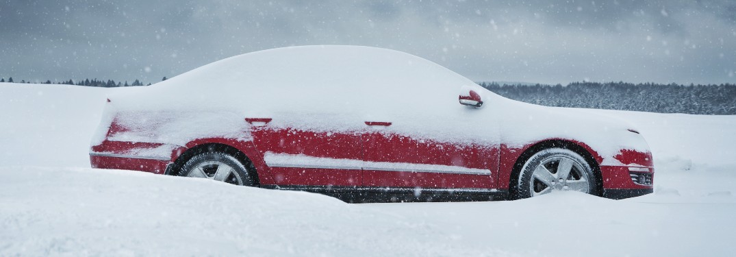 A red car parked in an open area with snow on top of it.