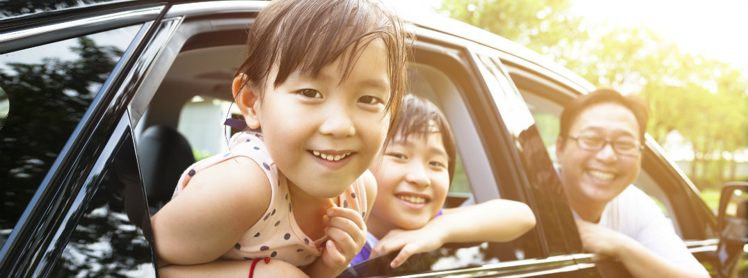 A happy girl and brother and father smiling out car windows