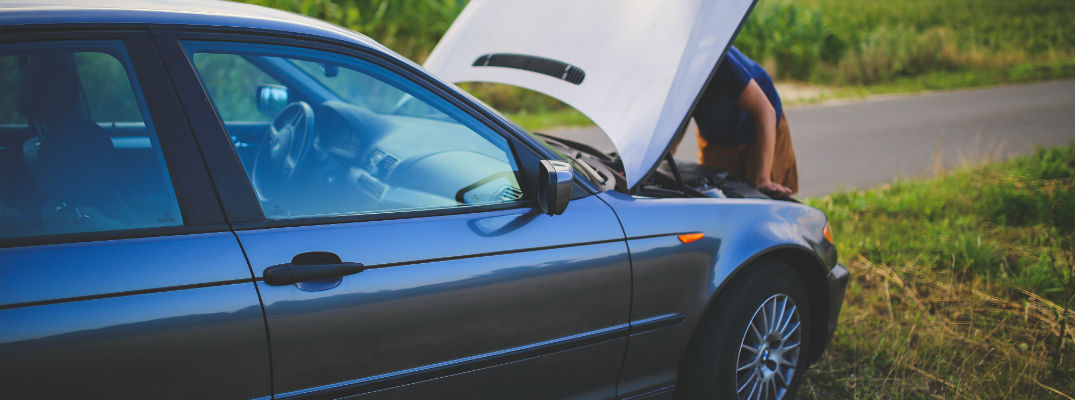 A stock photo of someone looking under the hood of a broken down car.
