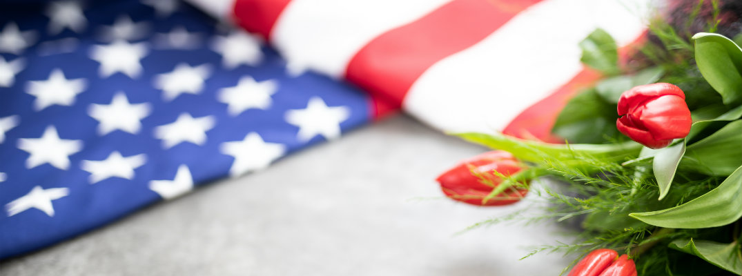 a folded American flag on the ground next to a bushel of red tulips